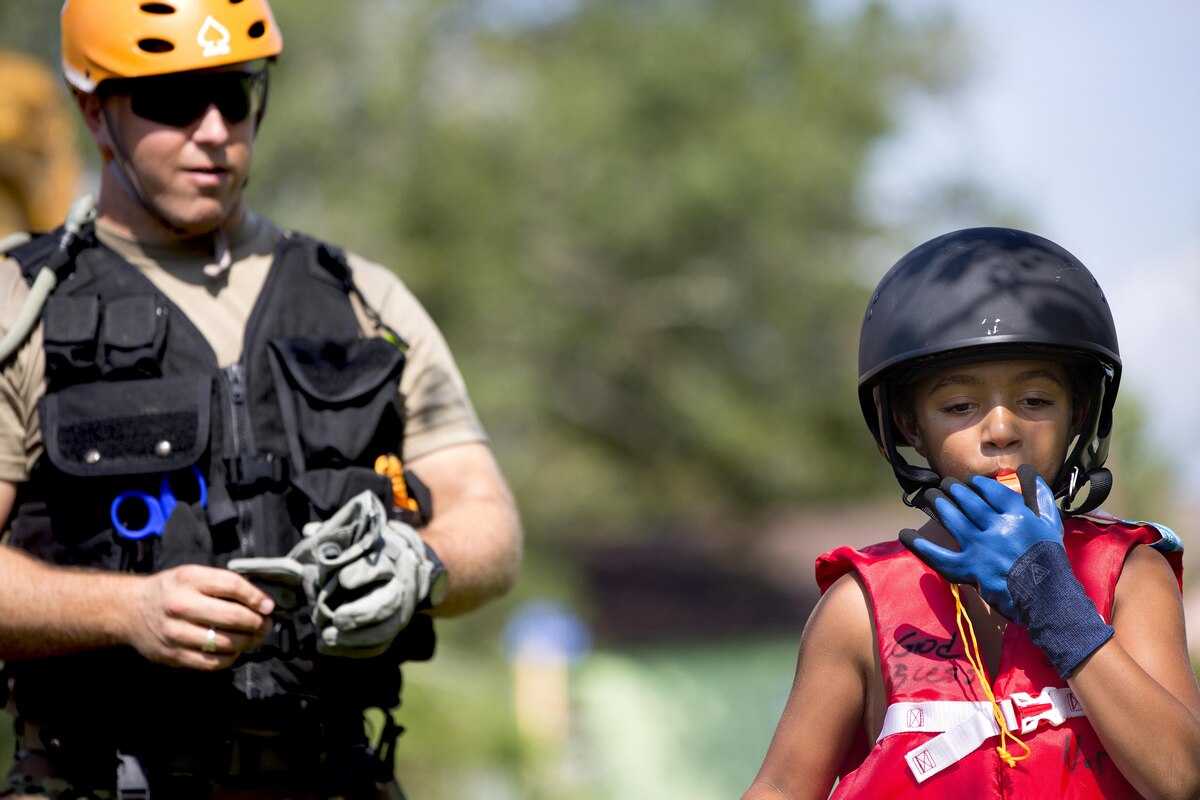 A child blows a whistle with a soldier nearby.