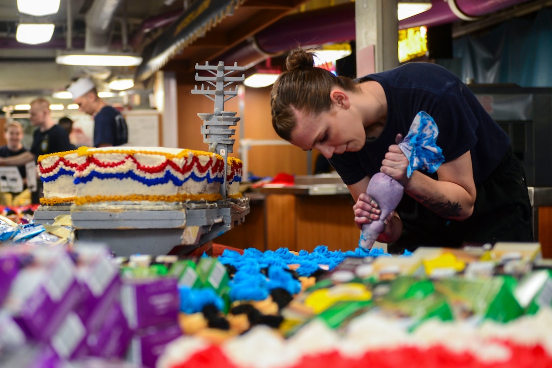 A sailor ices rows of cupcakes sitting on a table.