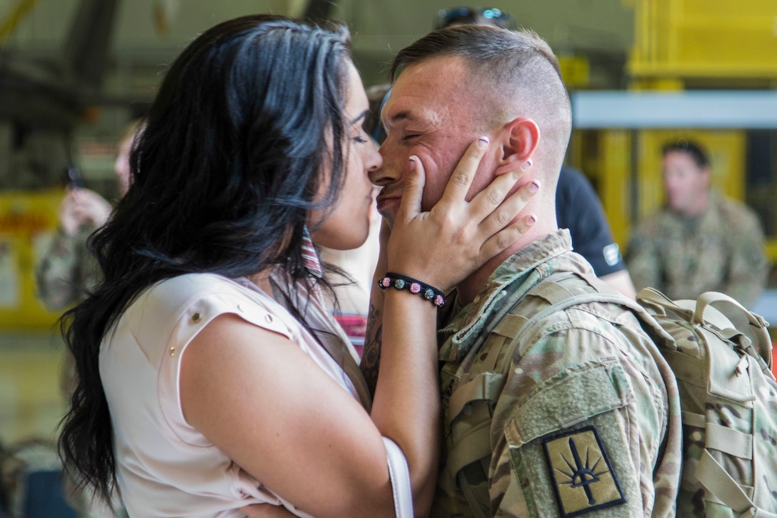 A woman prepares to kiss a soldier and embraces his face with both hands.