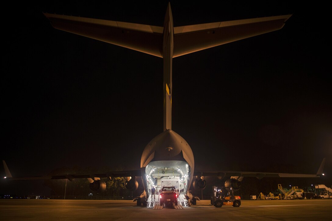 Airmen load supplies and equipment onto a C-17 Globemaster III at night.