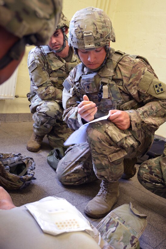 A soldier kneels down and writes on a piece of paper.