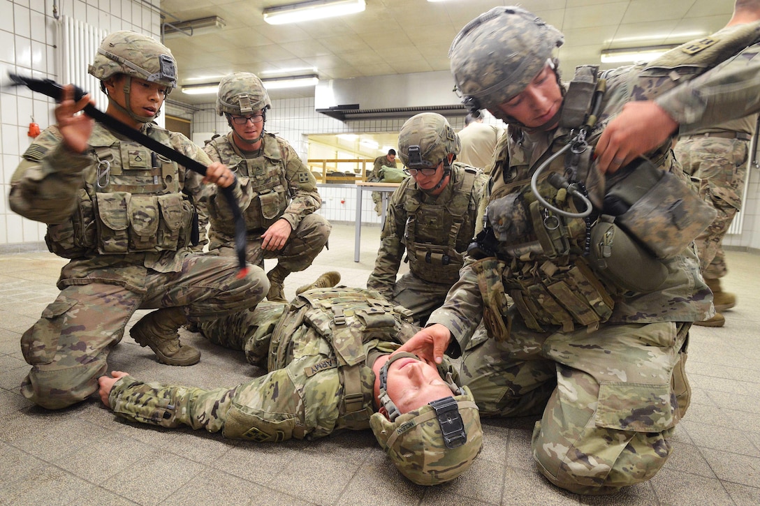 Four soldiers surround a manikin dressed as a soldier lying on the ground.