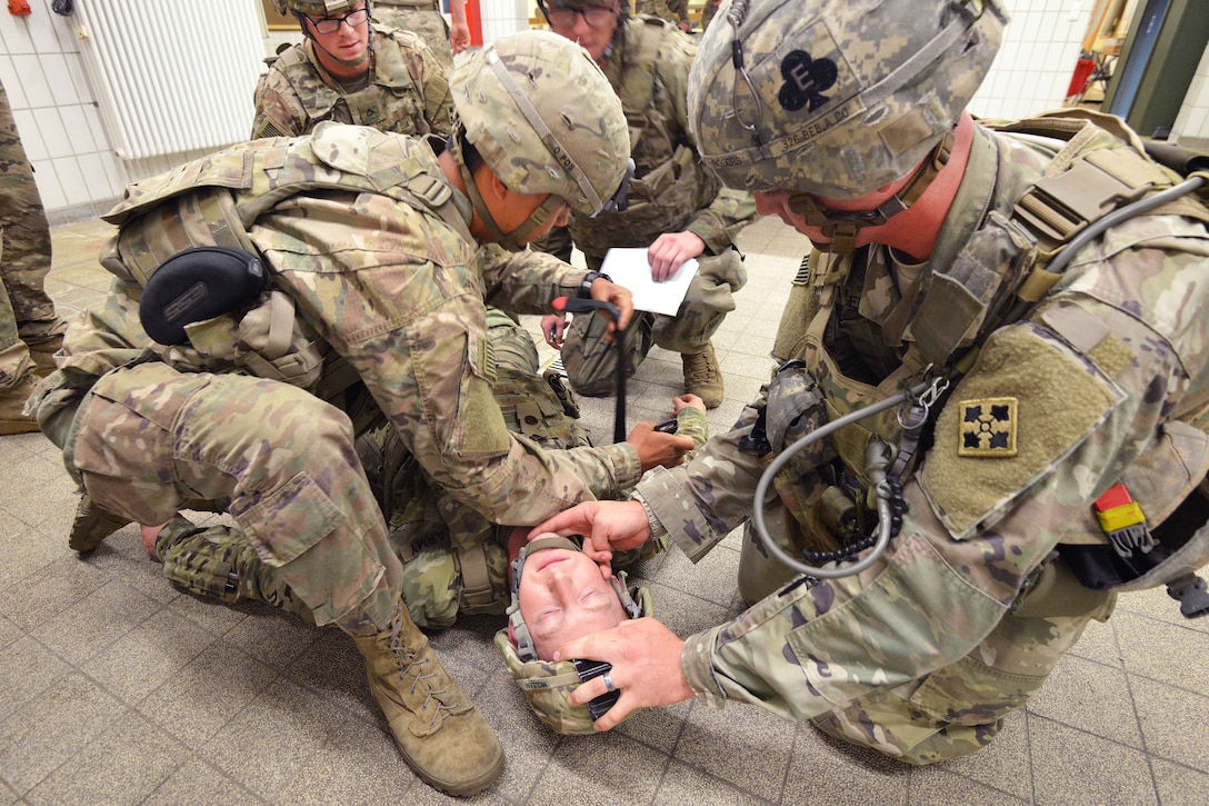 A group of soldiers lean over a manikin dresses a a soldier lying on the ground.