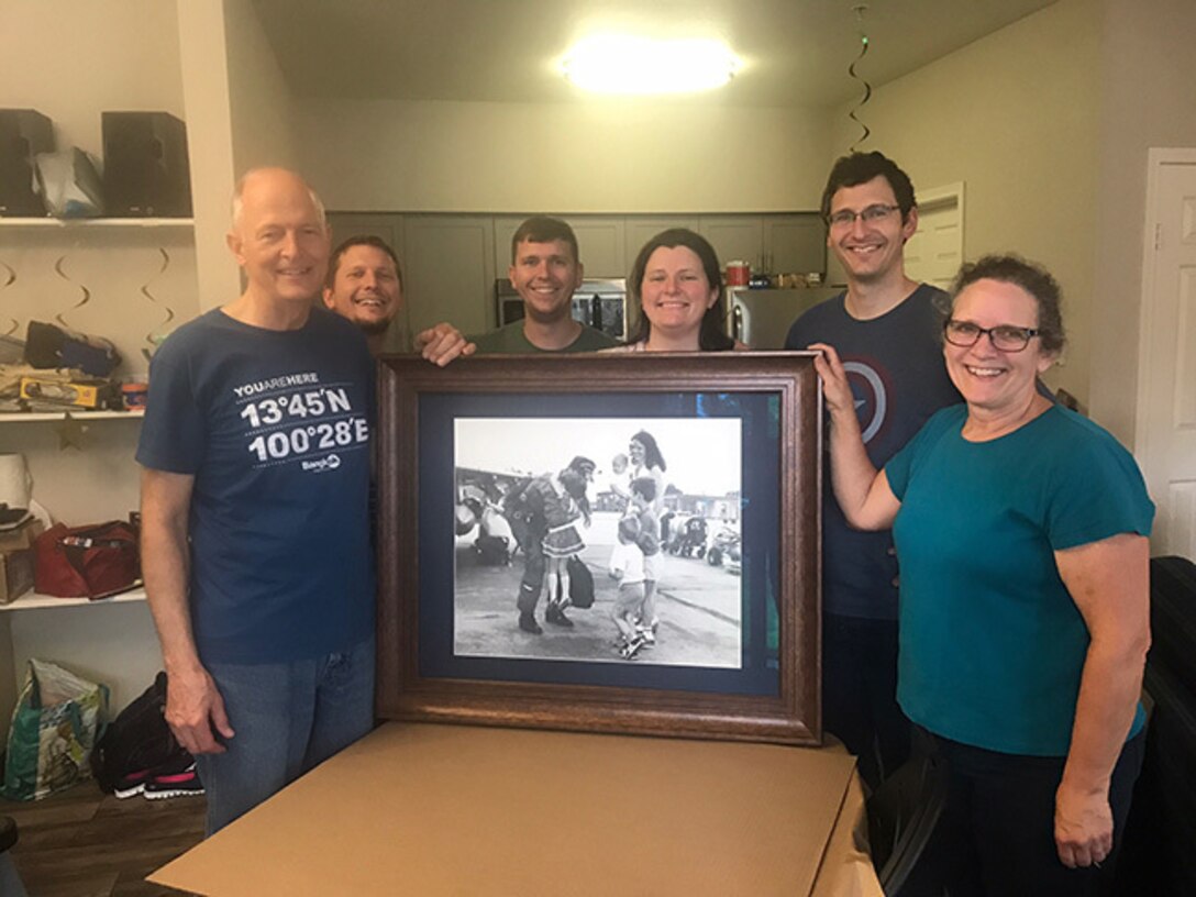 The Elliott family poses with their 1985 family portrait that shows retired Air Force Lt. Col. Gary, far left, being welcomed back to Moody Air Force Base, Ga., after a deployment, by his wife and children, June 18, 2017. After being notified of this portrait, the Elliot family searched for the photo for about 20 years. Upon receiving orders to Moody in 2015, Air Force Maj. Jonathan Elliott, 23rd Logistics Readiness Squadron director of operations, continued to search for the snapshot, obtaining it in 2016. Courtesy photo