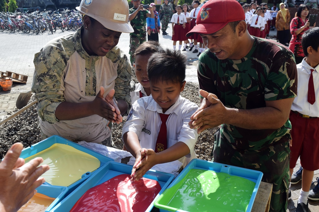 Navy Seaman Kiara Harris, assigned to Naval Mobile Construction Battalion 4, a local student and a member of an Indonesian marine battalion prepare to dip their hands in paint to leave their handprints on the schoolhouse that was built as part of the engineering civic action project during Cooperation Afloat Readiness and Training Indonesia 2016 in Surabaya, Indonesia, Aug. 30, 2016. The exercise's current iteration began Sept. 7, 2017. Navy photo by Petty Officer 3rd Class Santiago Guzman Jr.