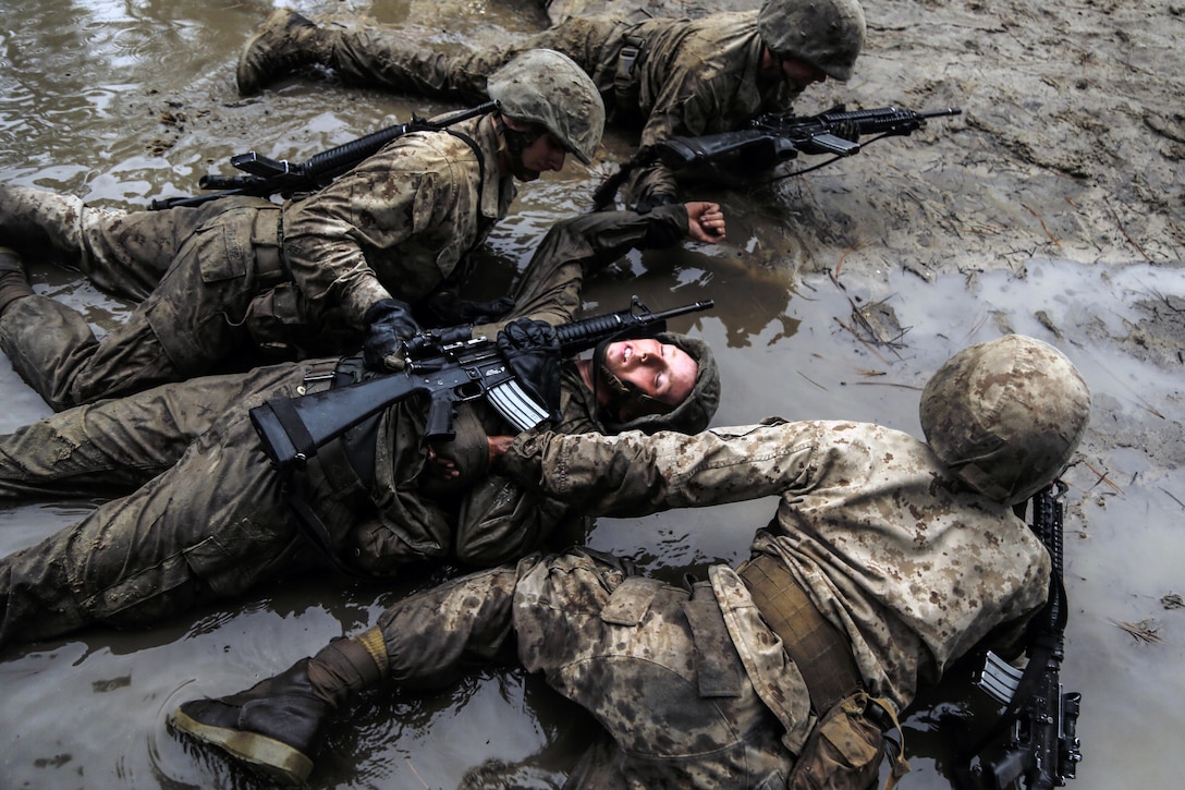 A group of Marines drag another Marine through the mud.