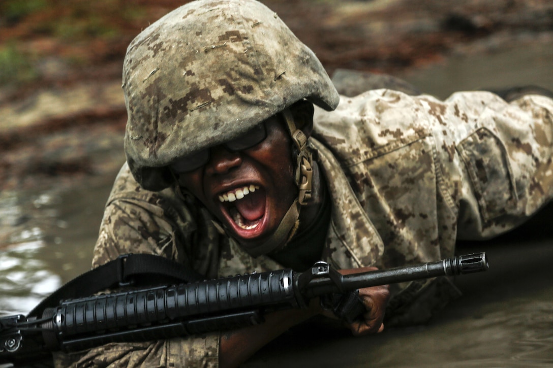 A Marine yells while crawling through the mud.