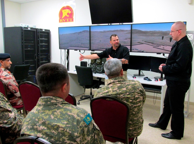 U.S. Army Soldiers sit in chairs watching two presenters in front of screens.