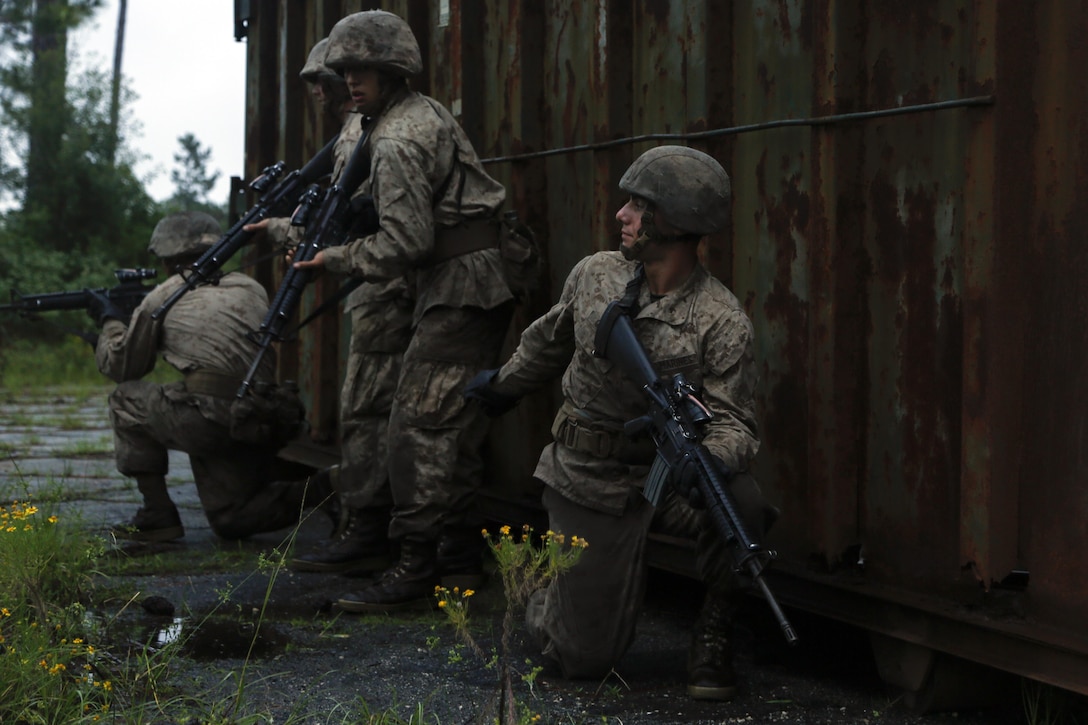 Three Marines stand and kneel behind a wall.