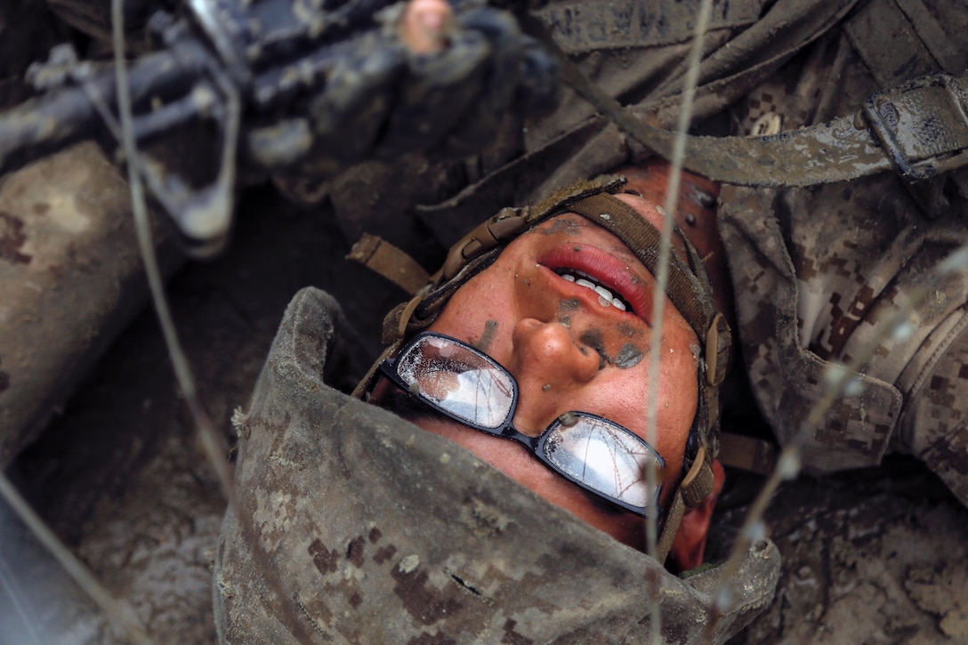 A Marine faces up while crawling under barbed wire.