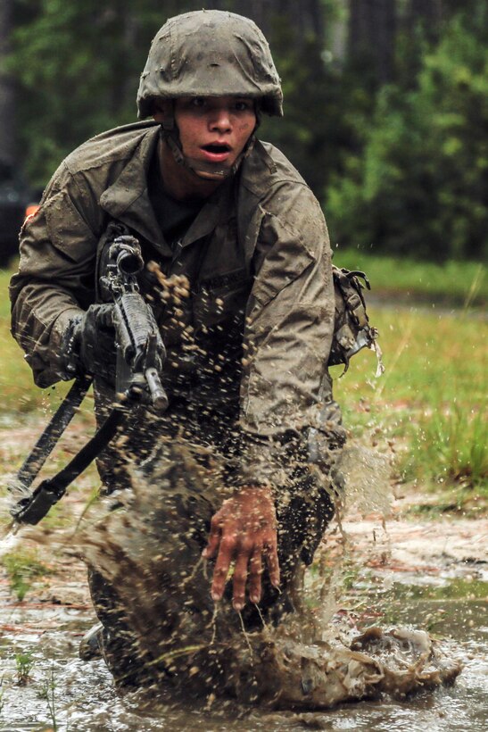 A Marine runs through knee deep, muddy water.