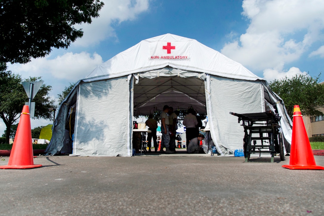 A tent with a red cross on the top sits in a parking lot.