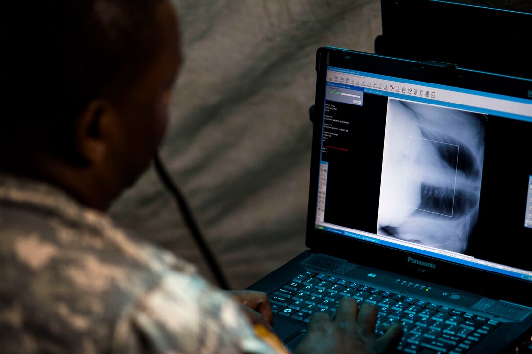 A service member looks at a computer with an image of an x-ray on the screen.