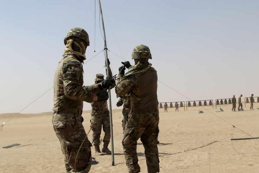 Three soldiers hoisting an antenna.