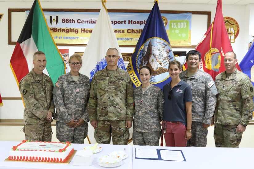 Civilians and U.S. army soldiers pose for photo in front of flags.