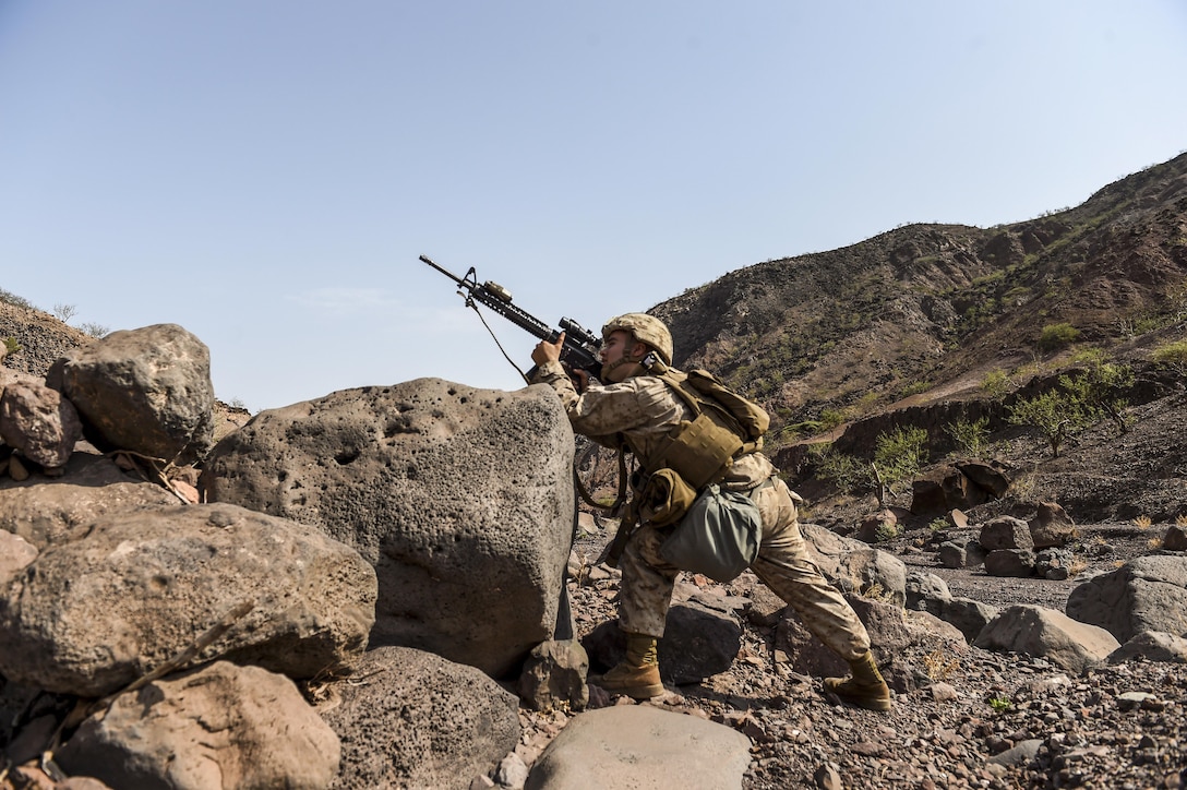A Marine aims his rifle up a rocky hill.