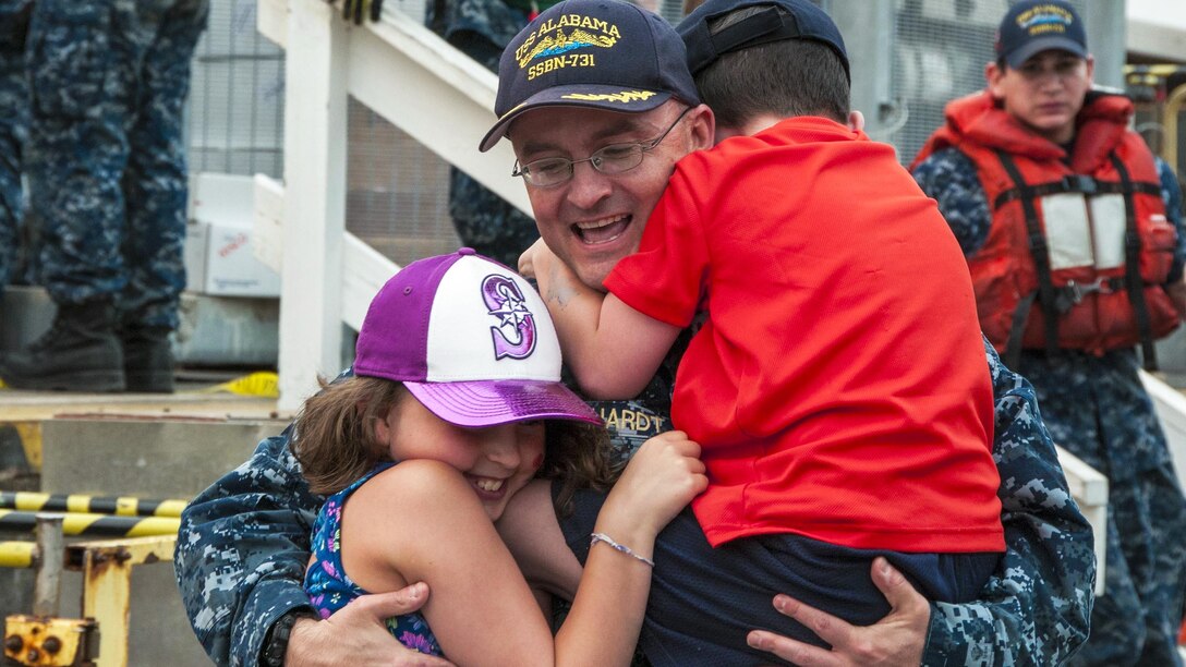 A sailor hugs his two children at a naval base.