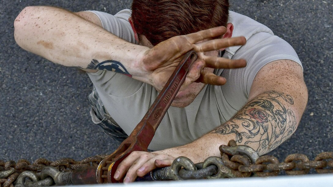 An airman tightens chains with a wrench that obscures his face.
