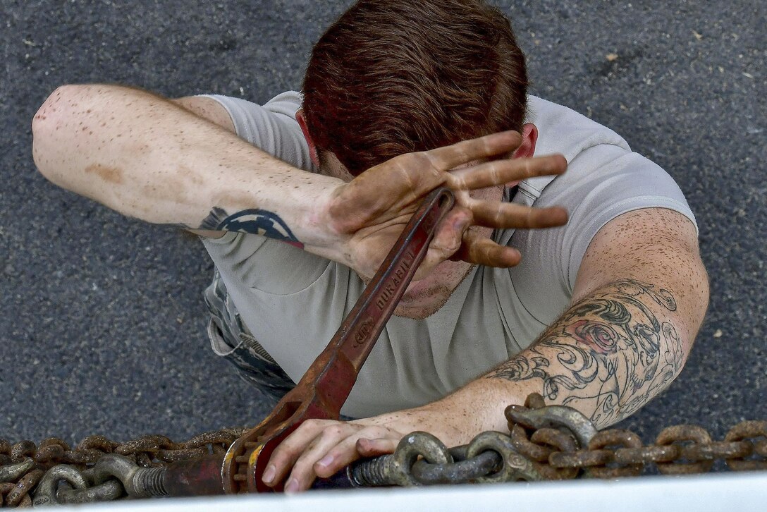 An airman tightens chains with a wrench that obscures his face.