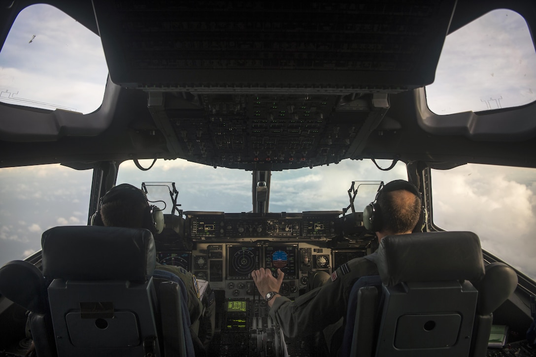 Two pilots look through an aircraft windshield while flying into clouds.