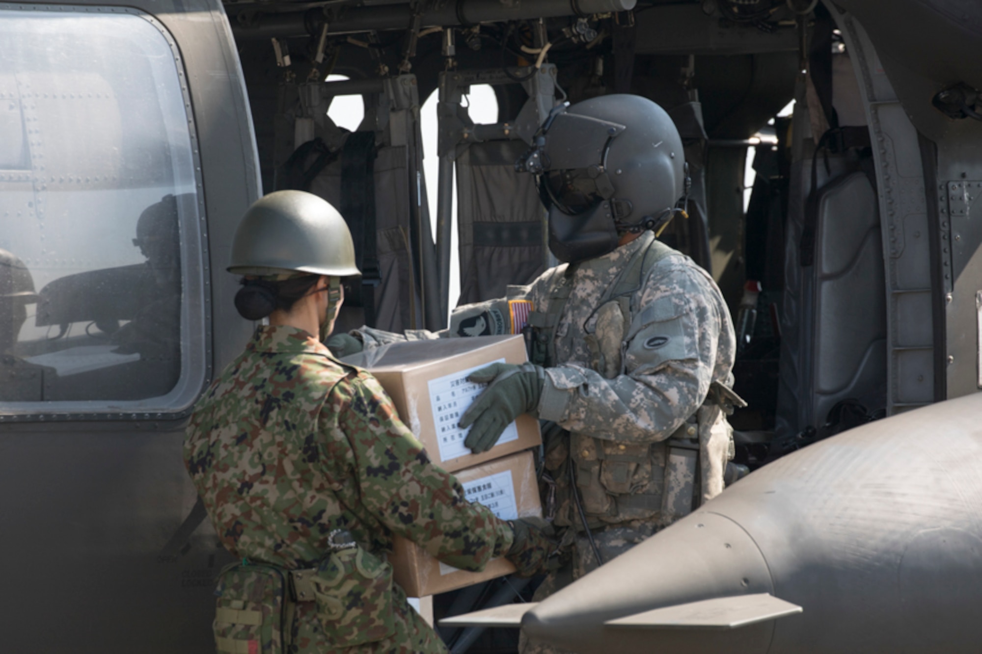 A U.S. Army UH-60 flight engineer passes simulated relief supplies to a Japan Ground Self-Defense Force member assigned to the 1st Logistics Regiment, JGSDF Nerima Station, at Yokota Air Base, Japan