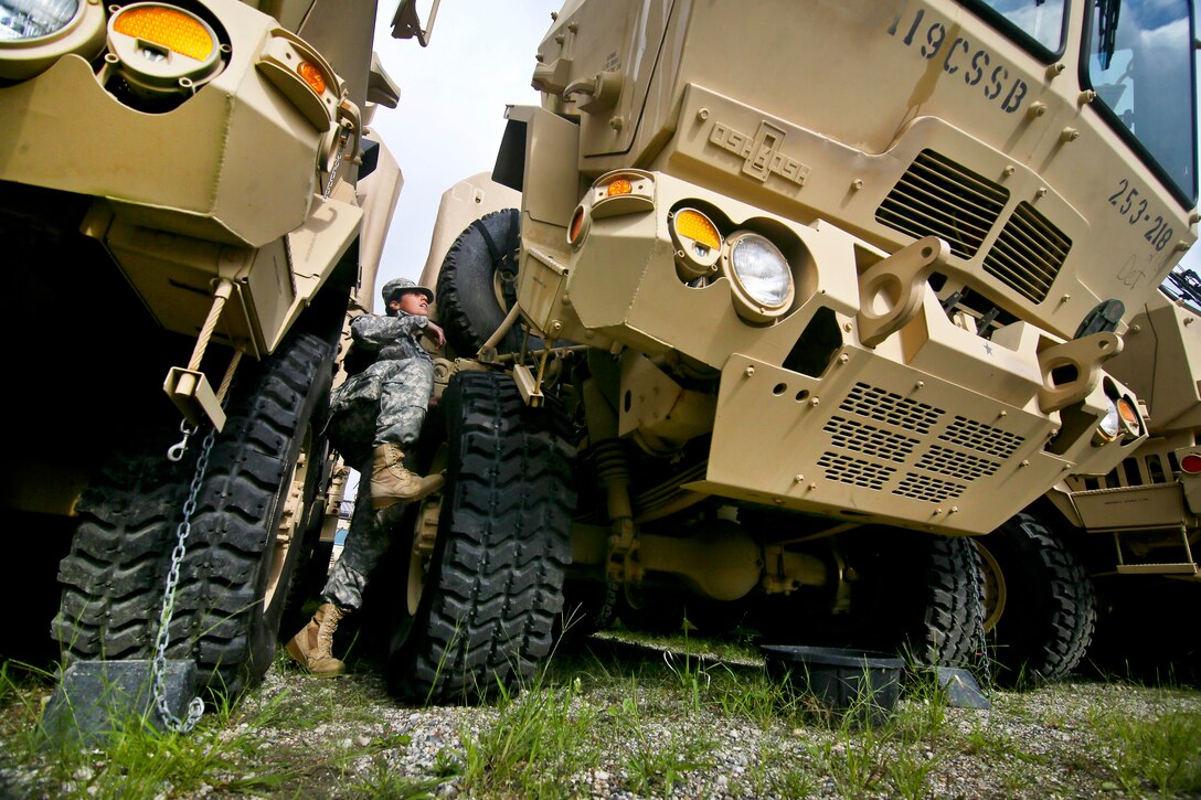 A soldier climes on a tire of a military vehicle.