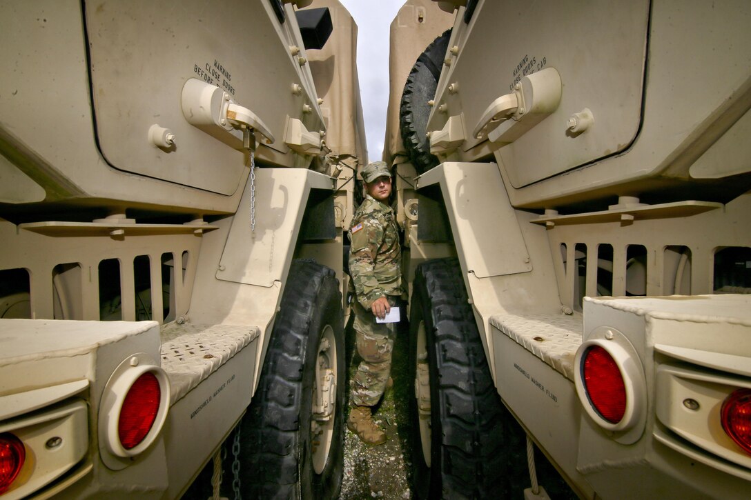 A soldier squeezes between two military vehicles to check the fuel.