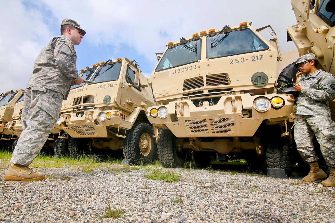Two guardsmen stand next to a row of military vehicles.