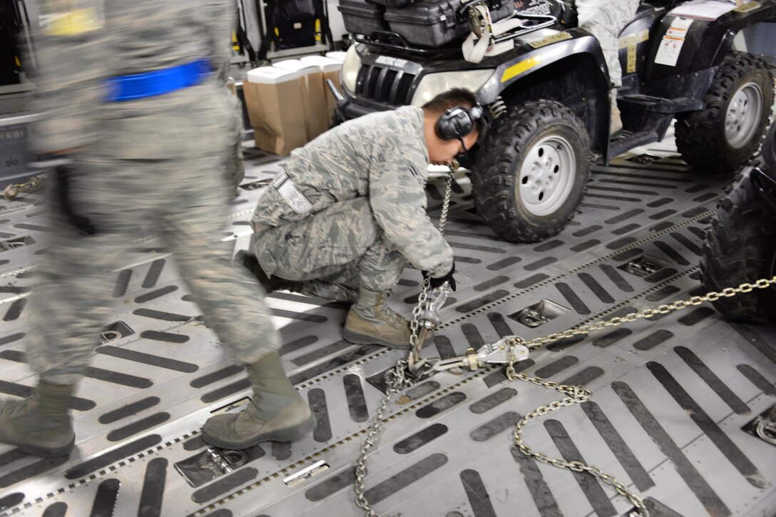 An airman tightens several chains securing vehicles and four supplies aboard a C-17 Globemaster III at Travis Air Force Base, Calif.