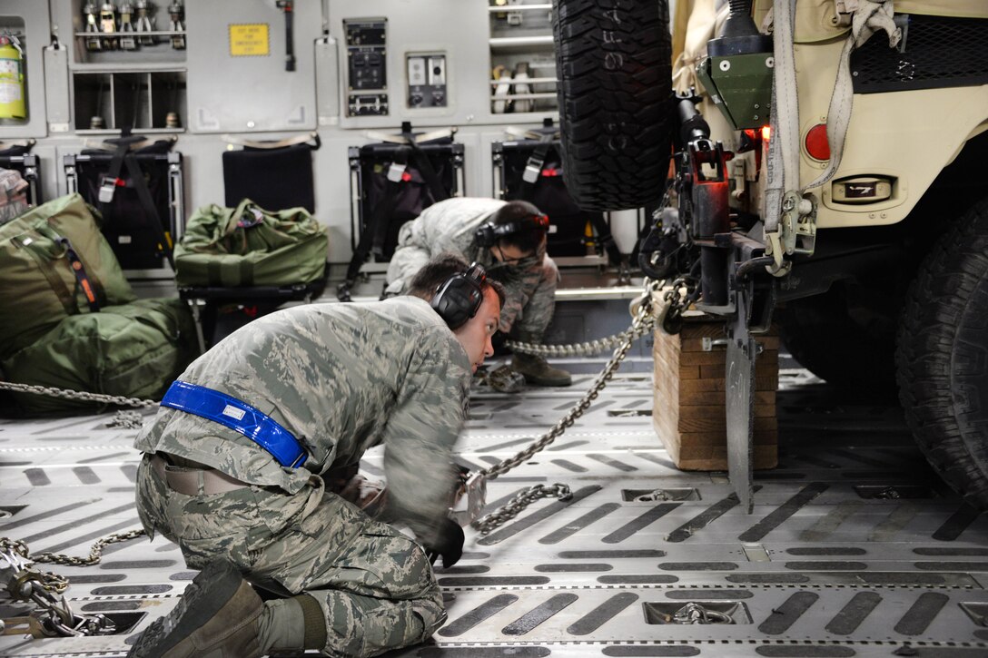 Airmen tighten chains securing a Humvee onto a C-17 Globemaster III