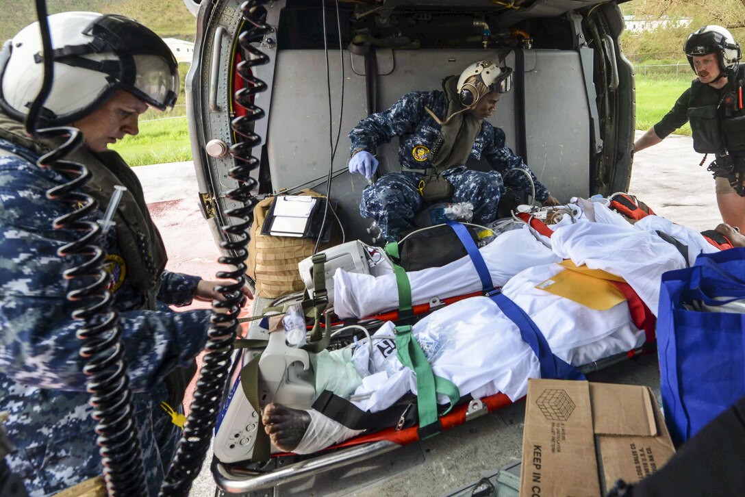Sailors assist patients on stretchers in a helicopter.