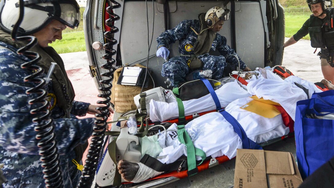 Sailors assist patients on stretchers in a helicopter.