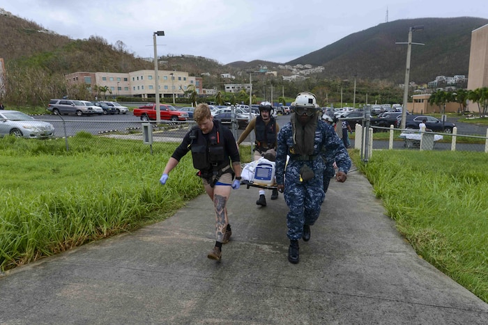 Sailors carry a person on a stretcher down a sidewalk.