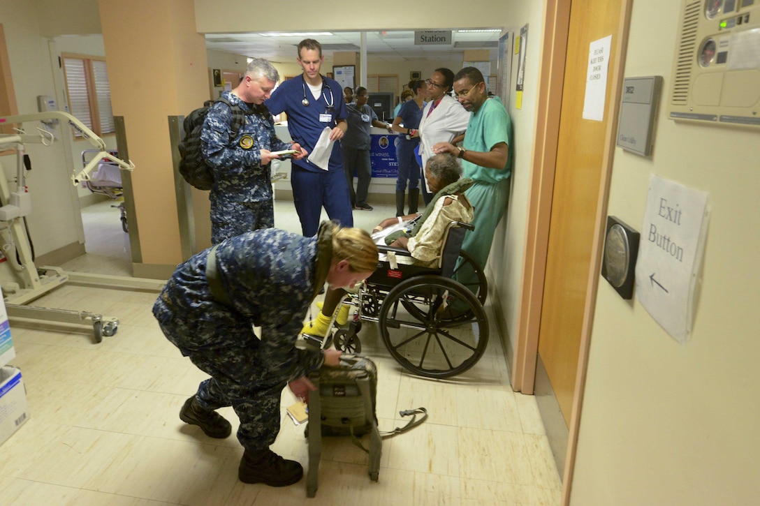 Two sailors speak to a group of people in the hallway of a hospital.