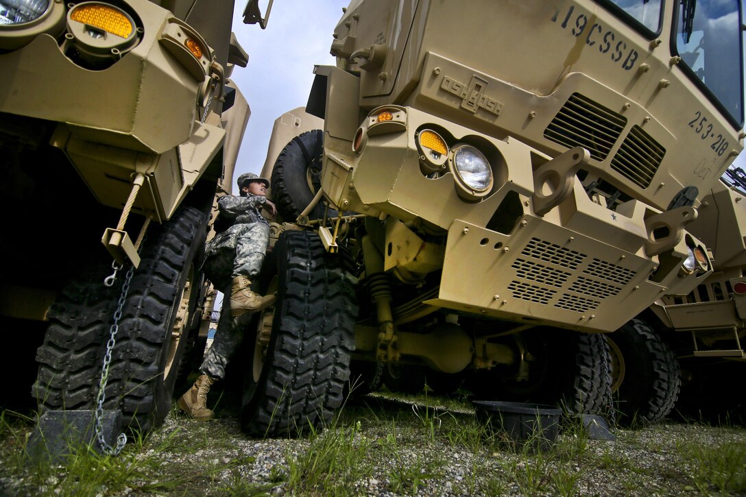 A soldier climbs on the tire of a large vehicle.