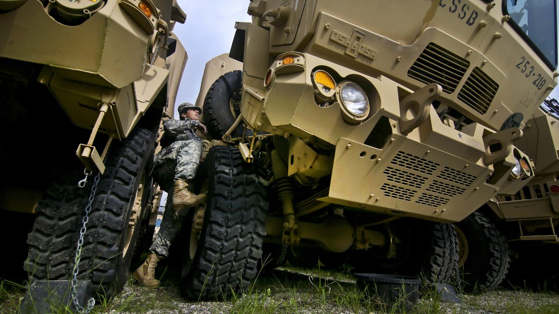 A soldier climbs on the tire of a large vehicle.