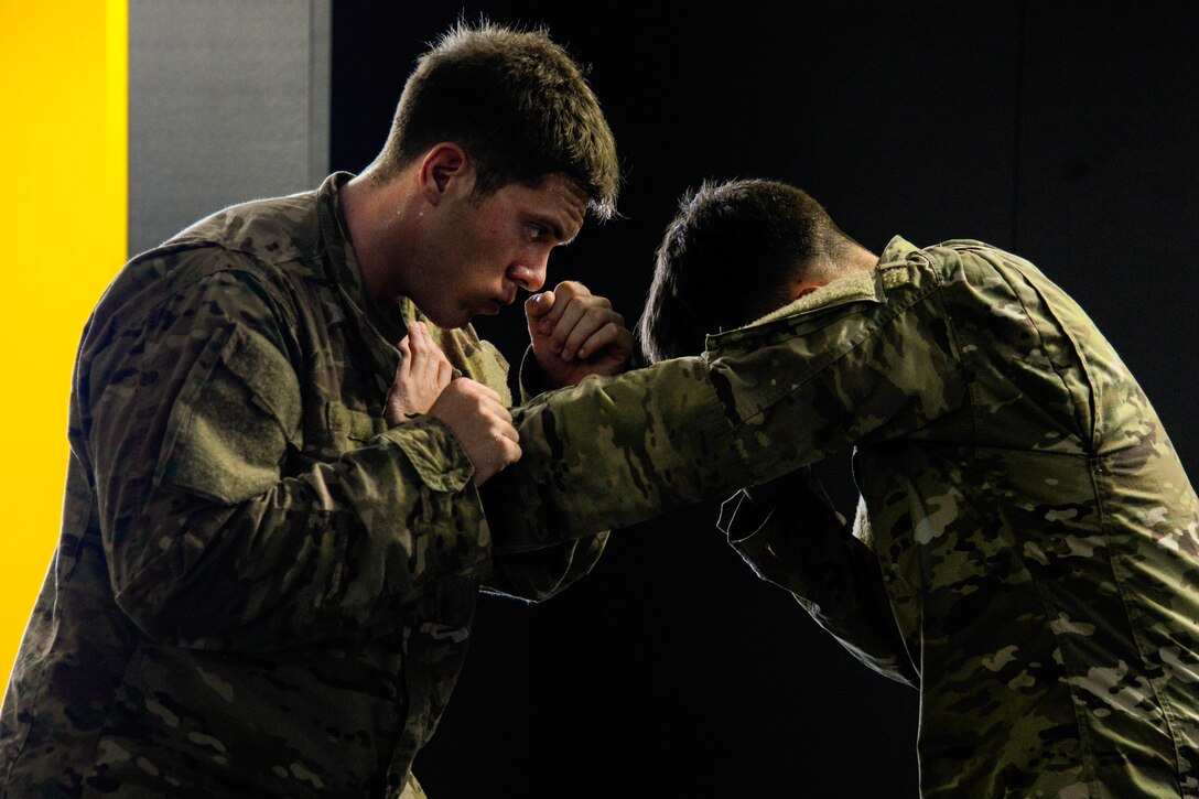 Two soldiers grapple with their hands while standing and facing each other.