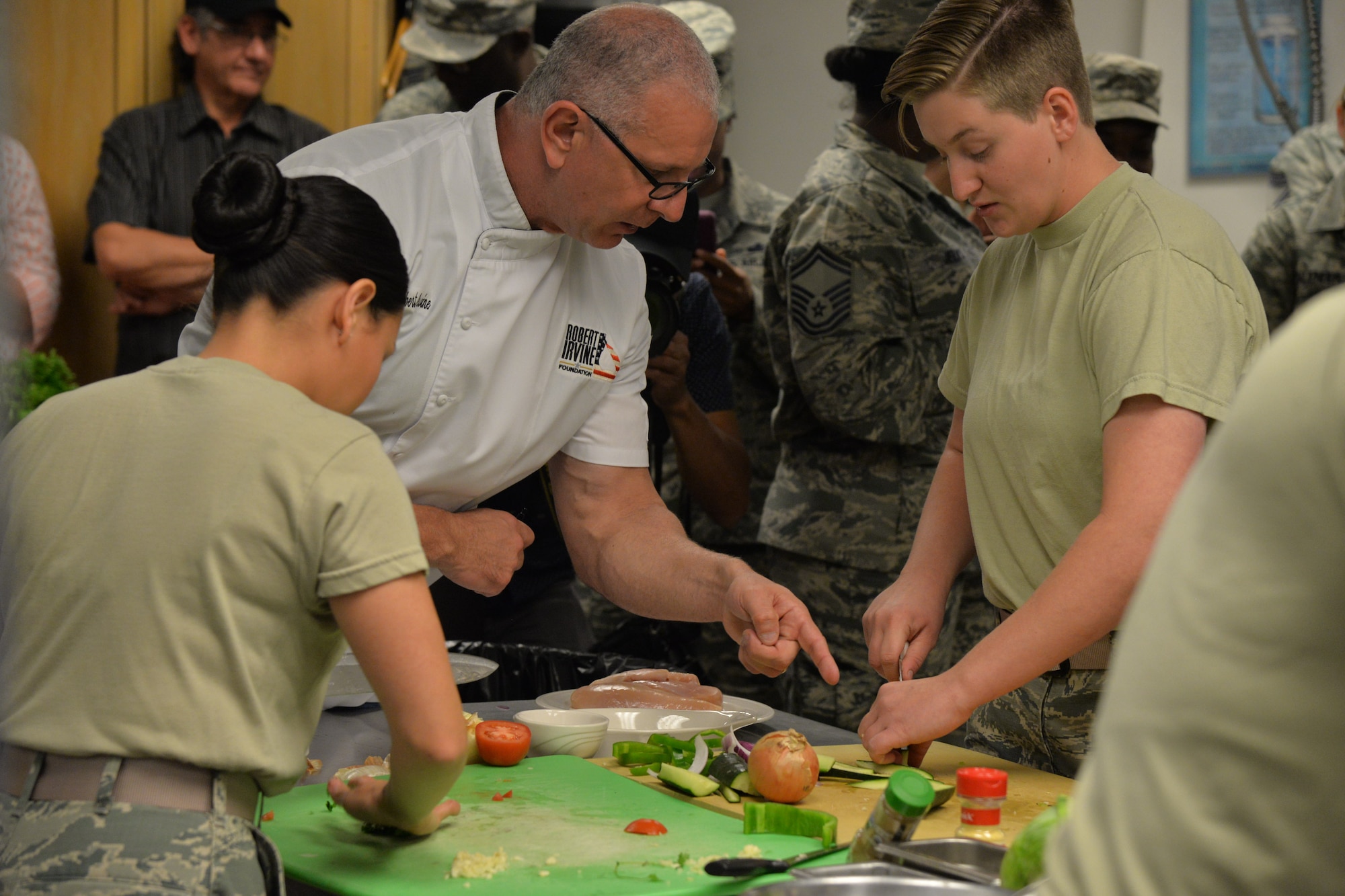 Celebrity Chef Robert Irvine assists Senior Airman Secilia Peraza, left, and Airman First Class Candance Ellenurg, both 90th Force Support Squadron missile field chefs, by coaching them as they prepare their individual dishes during a Warrior Chef Competition Sept. 7, 2017, at Malmstrom Air Force Base, Mont. Chef Irvine was a mentor and a judge for the competition.  (U.S. Air Force phot/Airman First Class Daniel Brosam)