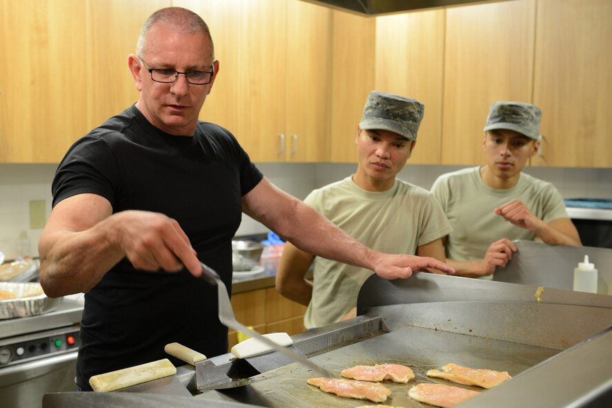 Celebrity Chef Robert Irvine shows Airman First Class Nicki Agunos, center, and Senior Airman Salvador Argumedo, both 341st Force Support Squadron missile field chefs, how to quickly improve the quality and taste of grilled chicken while preparing lunch Sept. 6, 2017, at a missile alert facility near Ulm, Mont. Chef Irvine visited a MAF to better understand the unique challenges missile chefs face and provided feedback on ideas for improving the meal process. (U.S. Air Force photo/Staff Sgt. Delia Martinez)