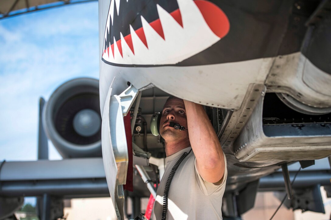 An airman reaches up into an aircraft with a mouth with sharp teeth painted on its nose.