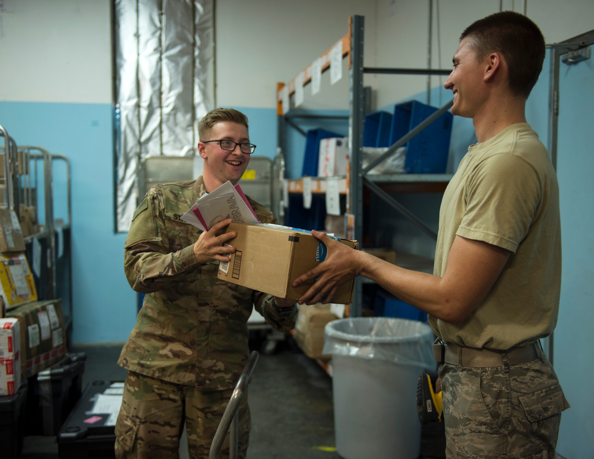 U.S. Air Force Airman 1st Class Kevin Otero, right, a military postal clerk with the 379th Expeditionary Communication Squadron, hands off a care package to a customer at Al Udeid Air Base, Qatar, July 14, 2017.
