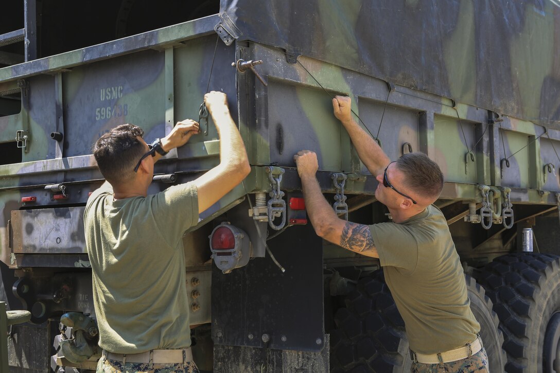 Two Marines secure a tarp onto a truck.