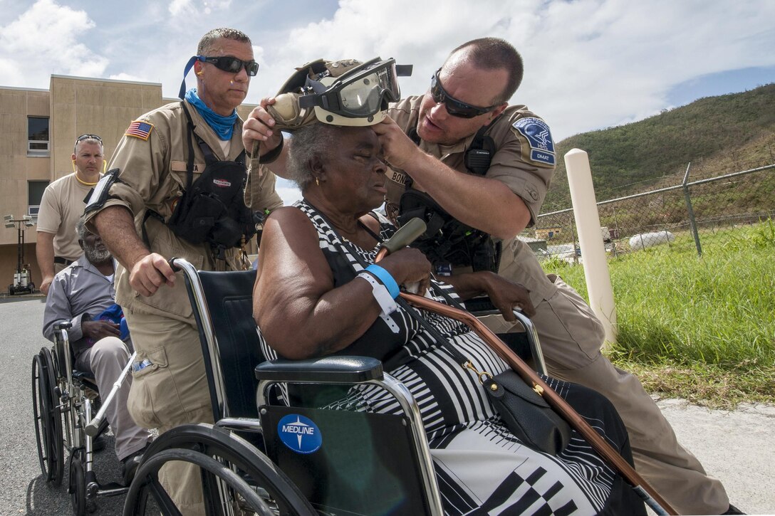 A man helps a woman in a wheelchair put on protective eye wear.