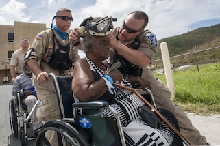 A man helps a woman in a wheelchair put on protective eye wear.