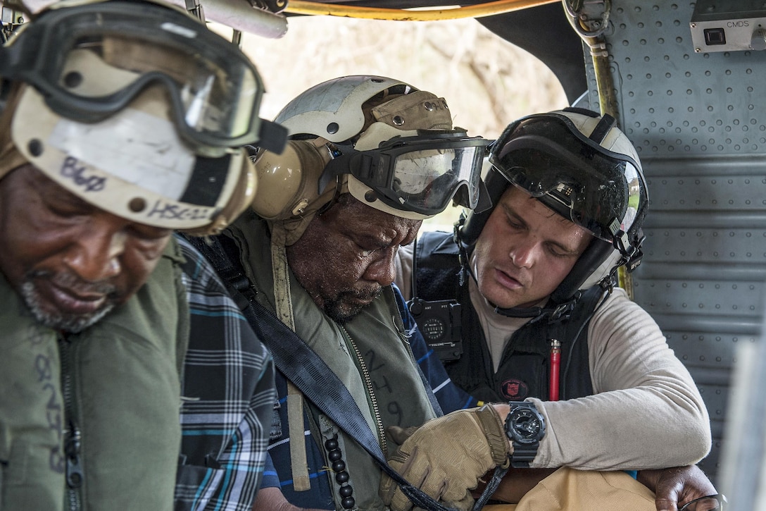 A sailor helps strap in a civilian aboard a helicopter