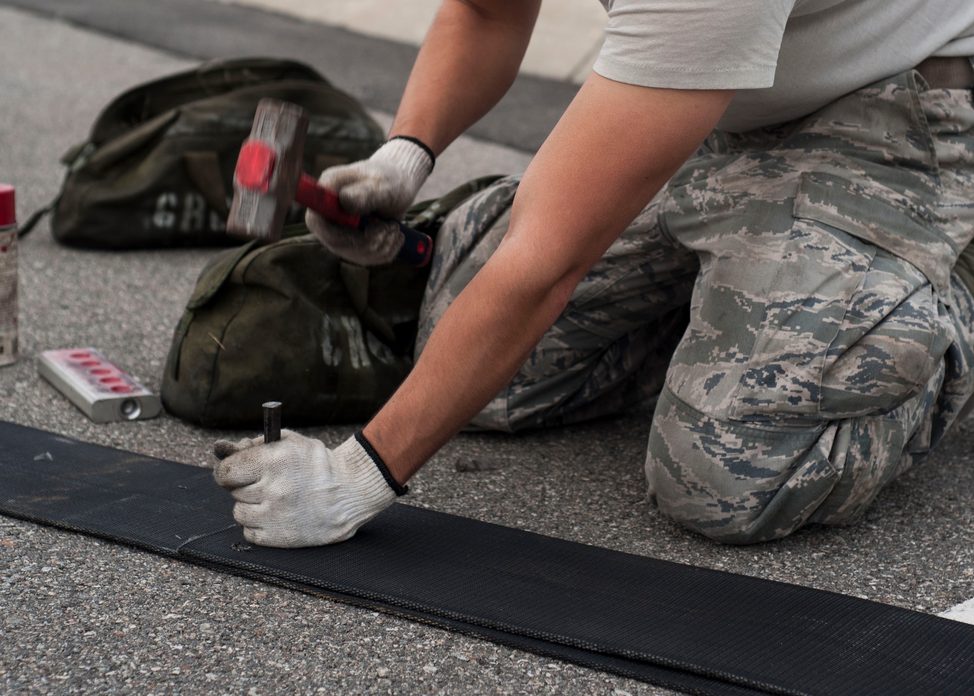 U.S. Air Force Senior Airmen Daniel Tomasek, 8th Civil Engineer Squadron electrical power production journeyman, uses a hammer to pierce holes in the nylon tape used for the aircraft arresting system at Kunsan Air Base, Republic of Korea, Sept. 9, 2017. The holes allow for the attachment of a connector that hooks to a steel cable strung across the flight line. The system, which is designed to bring out-of-control aircraft to a safe stop, can withstand a tension of approximately 170 pounds per square inch. (U.S. Air Force photo by Staff Sgt. Victoria H. Taylor)