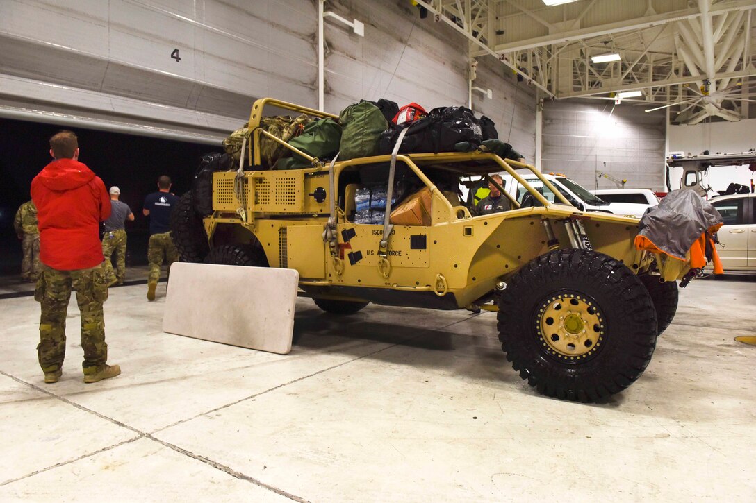 Coast Guard and Air Force personnel organize supplies and gear near a military vehicle.