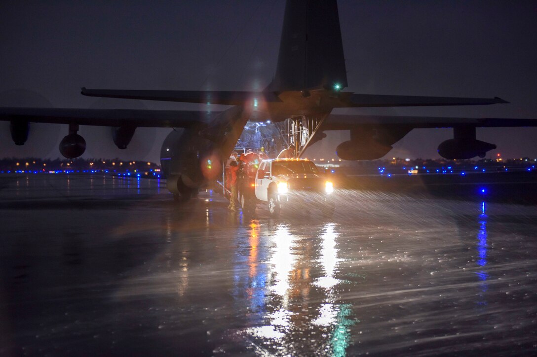 Coast Guard and Air Force personnel offload supplies and gear from an airplane at night.