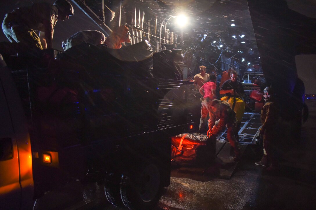 Coast Guard and Air Force personnel offload supplies and gear from an aircraft at night.