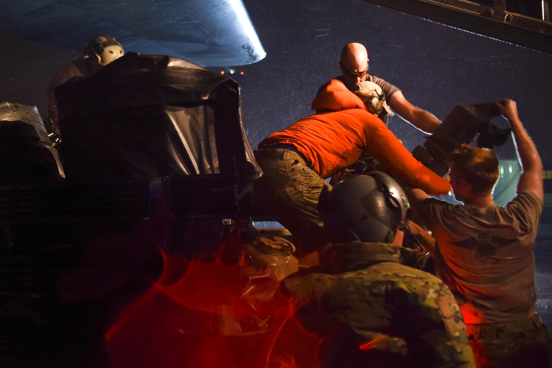 Coast Guard and Air Force personnel offload supplies and gear from an aircraft at night.